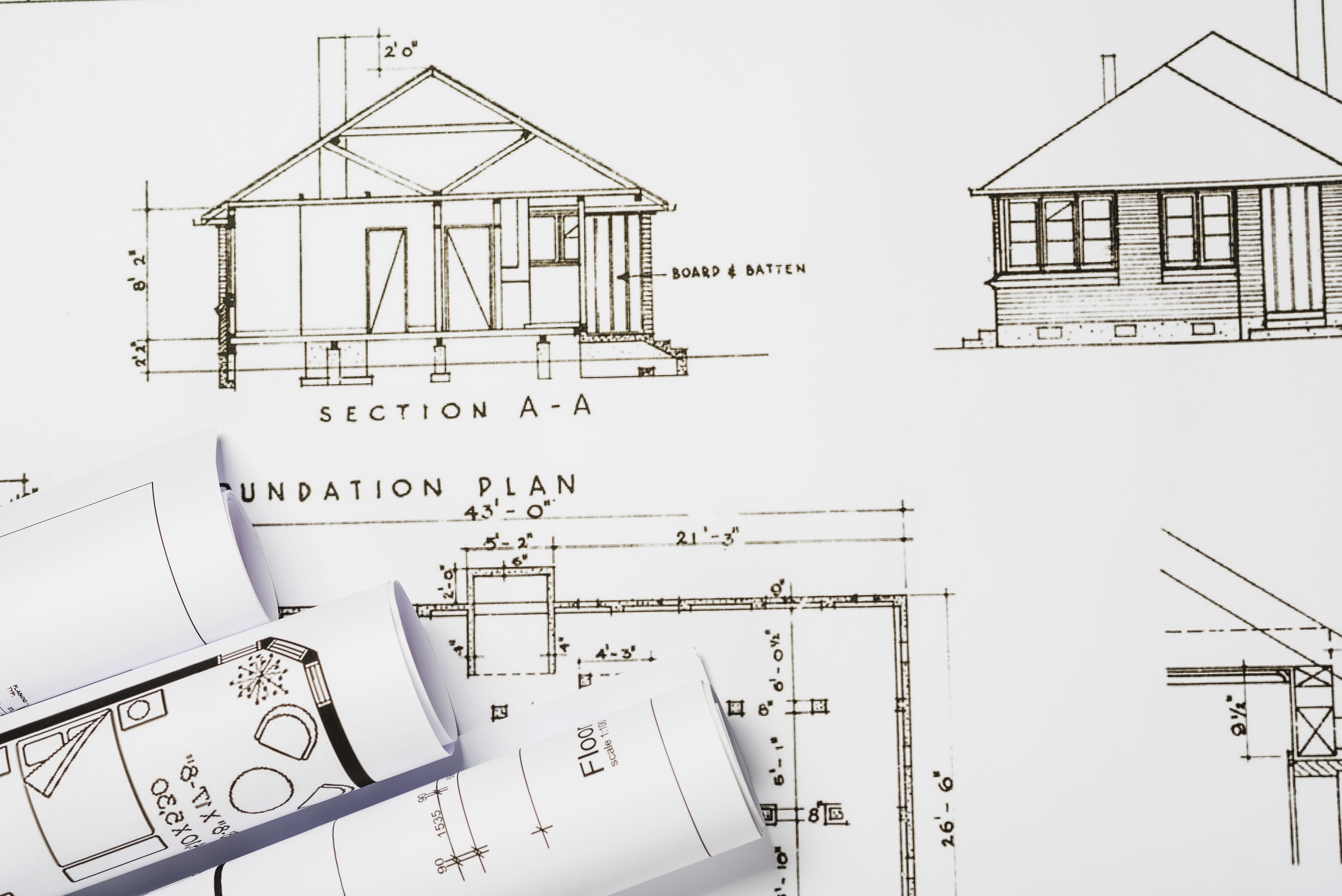 Here, a set of architectural drawings of a house created by one of the Reliable Architects in the Hamilton Region can be seen.  Also appearing are a set of 3 rolled up blueprint drawings laying on top of the original plans..