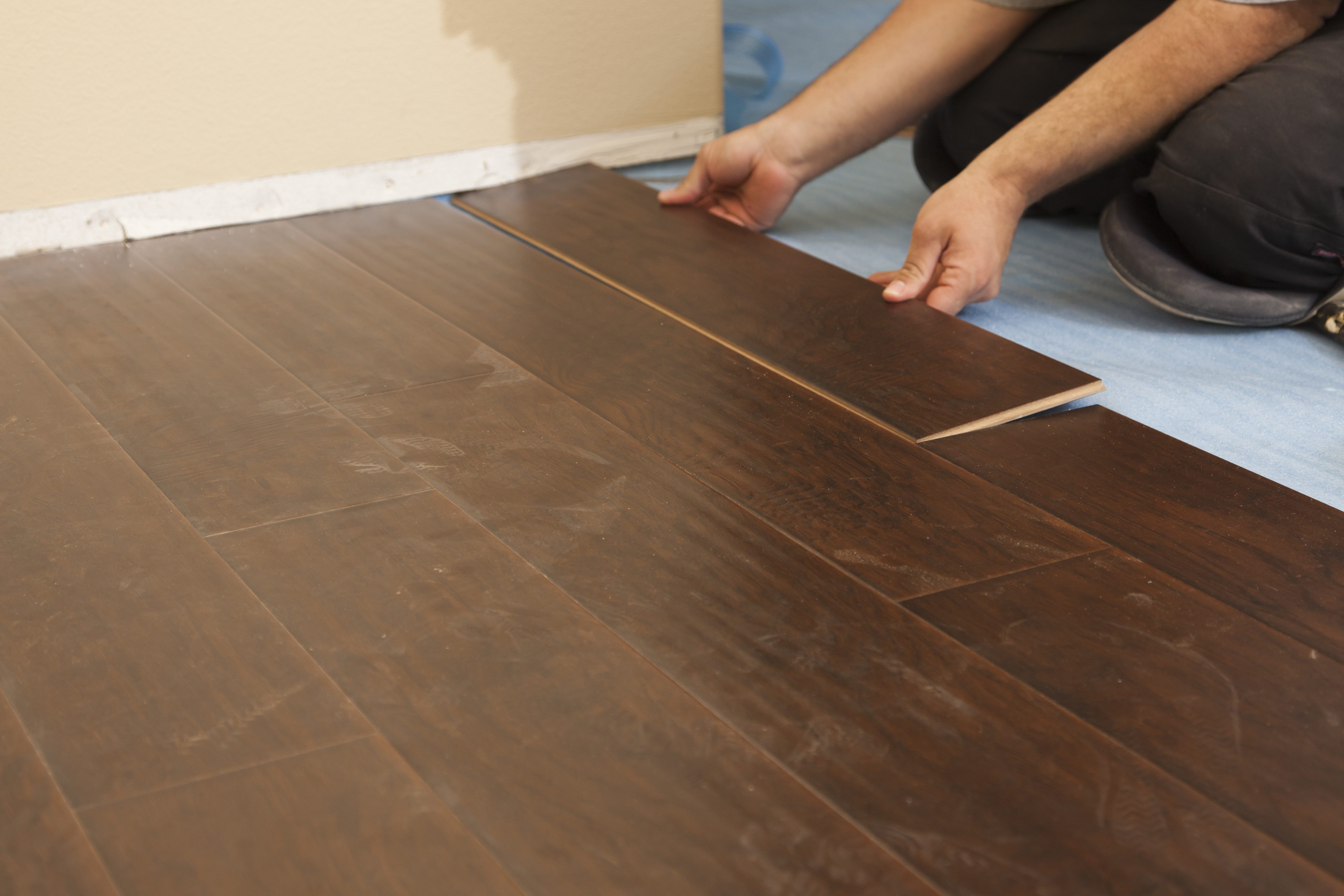 One of the Top-Rated Flooring Installers in Ottawa is kneeling down and interlocking a coffee coloured click system tongue and groove laminate flooring product together.