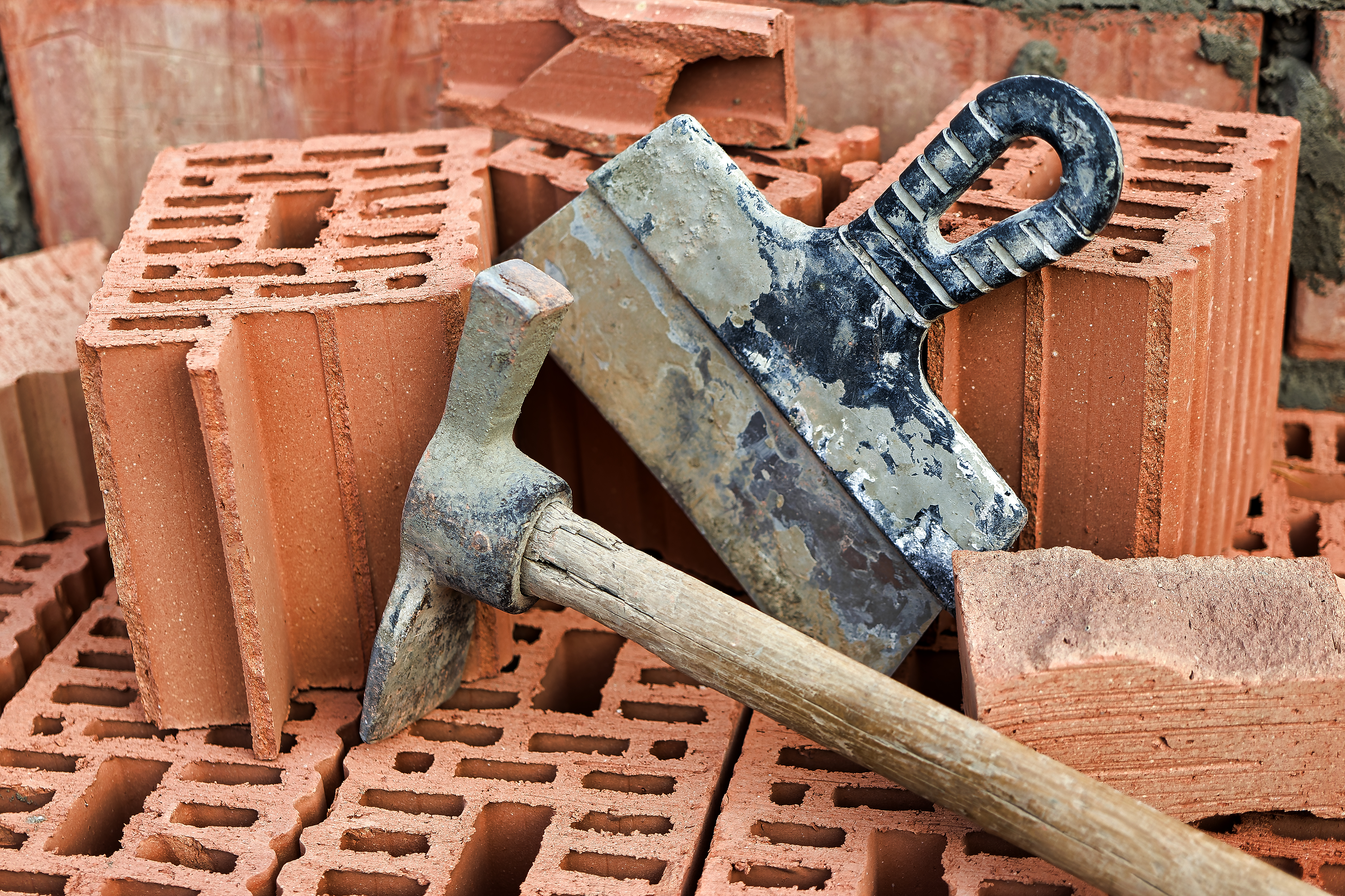Tools that some of the Best Masons in Ottawa use. This image shows a pile of red bricks with a trowel and masons’ hammer staged for the photo, against a top row of bricks.